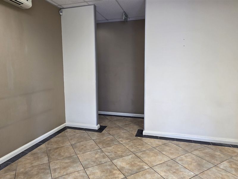 An empty office space featuring tiled flooring, neutral wall tones, and an integrated air conditioning unit, suitable for a professional workspace.