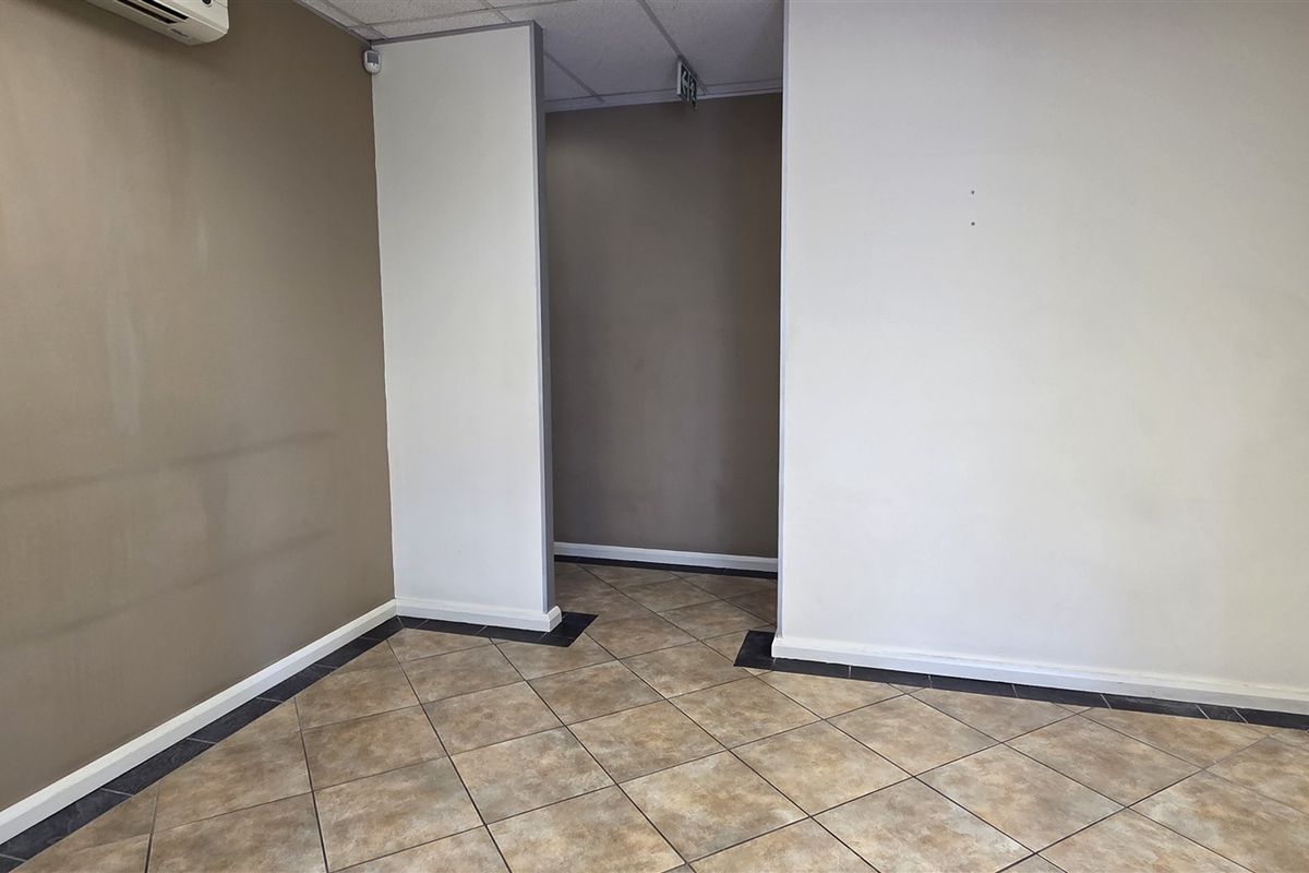 An empty office space featuring tiled flooring, neutral wall tones, and an integrated air conditioning unit, suitable for a professional workspace.