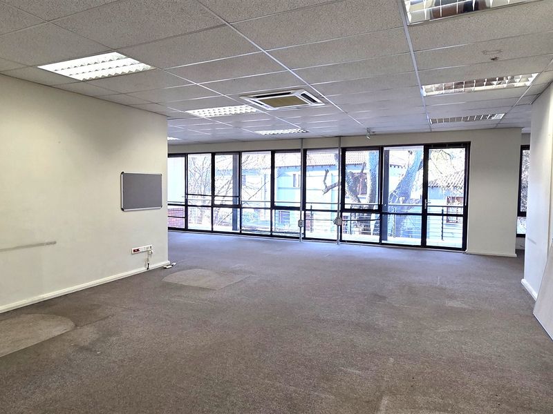 Spacious open-plan office area featuring large windows for natural light, suspended ceilings with integrated lighting, and central air conditioning.