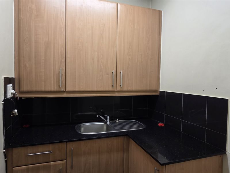 A functional scullery area featuring wood-finish cabinetry, a stainless steel sink, and a black tiled backsplash with a dark countertop.
