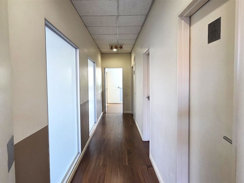 A clean, well-lit office hallway featuring laminate flooring, suspended ceiling tiles, and multiple access doors leading to individual office spaces.