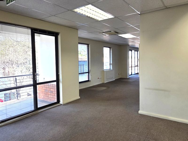 Spacious, open-plan office area featuring large windows with natural light, suspended ceilings, and carpeted flooring, suitable for a professional workspace.