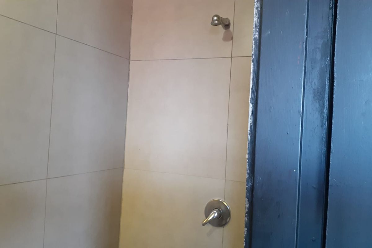 A shower enclosure featuring wall-mounted shower head and mixer tap, finished with neutral wall tiles and a dark painted door frame.