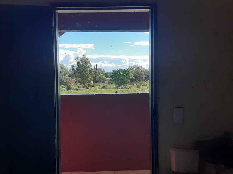 An interior view looking through an open doorway towards an outdoor landscape, showing signs of significant wear and maintenance requirements.