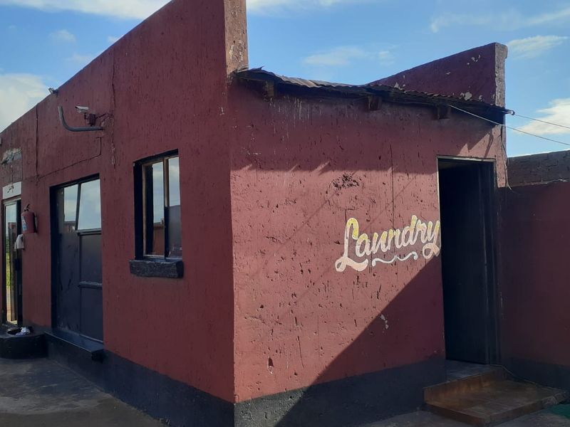 Exterior view of a standalone laundry facility featuring a painted masonry structure with a dedicated entrance and window.