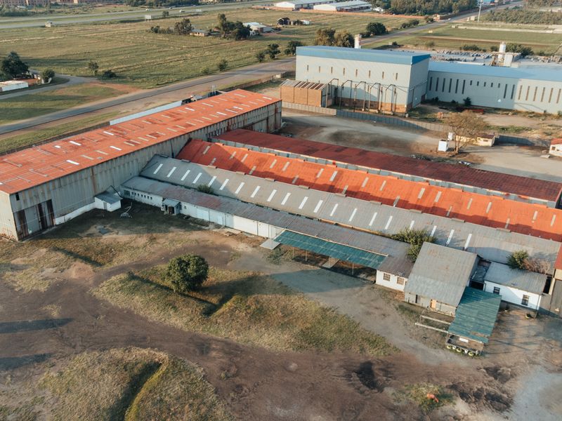 Aerial view of a large industrial facility featuring extensive warehouse structures with metal roofing and surrounding open yard space.