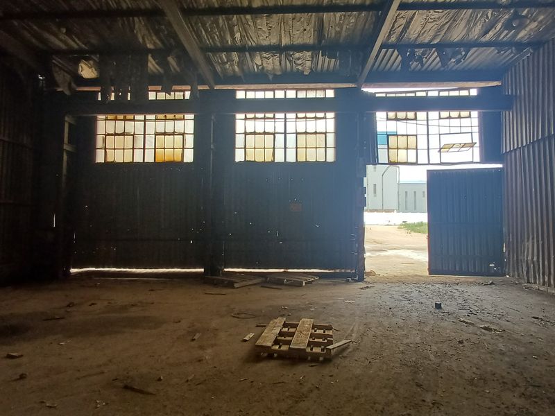 Spacious industrial warehouse interior featuring high ceilings, corrugated metal walls, and large access doors, offering a versatile open-plan workspace.
