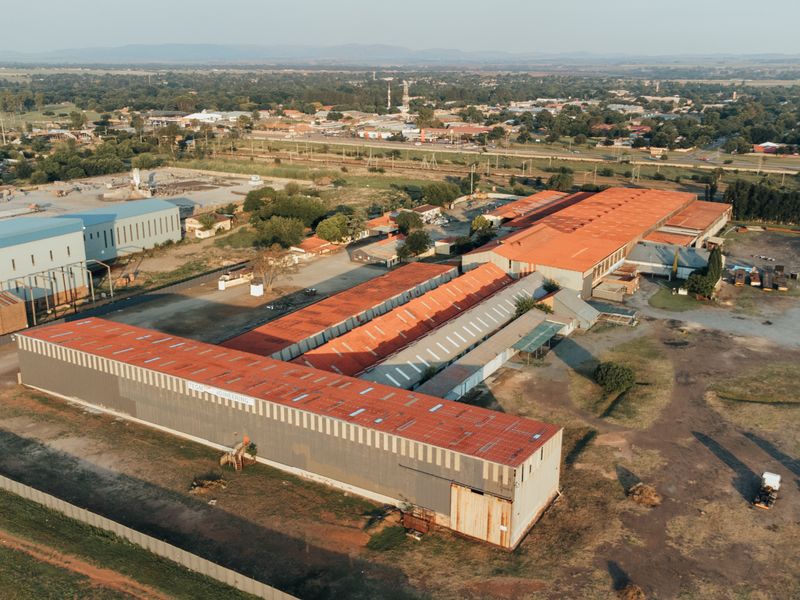 Aerial view of a large industrial facility featuring multiple expansive warehouse structures with metal roofing and surrounding open yard space.