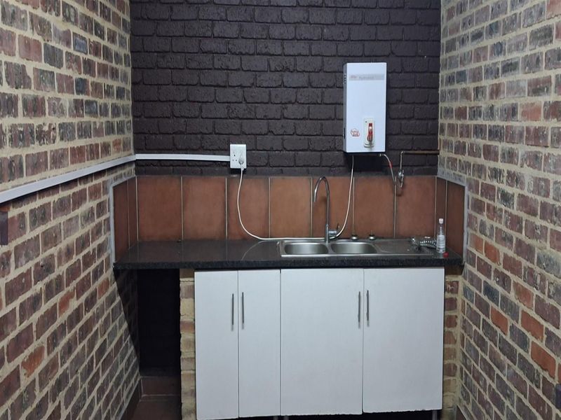 A functional scullery area featuring exposed brick walls, granite countertops, a stainless steel double sink, and built-in cabinetry with an electric water heater.