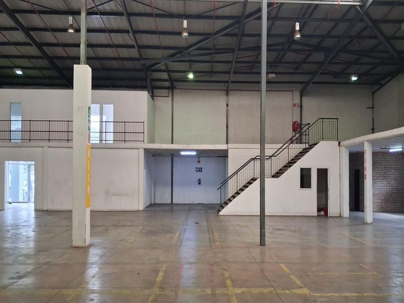 Spacious industrial warehouse unit featuring a mezzanine level, concrete flooring, exposed steel roof structure, and internal staircase access.