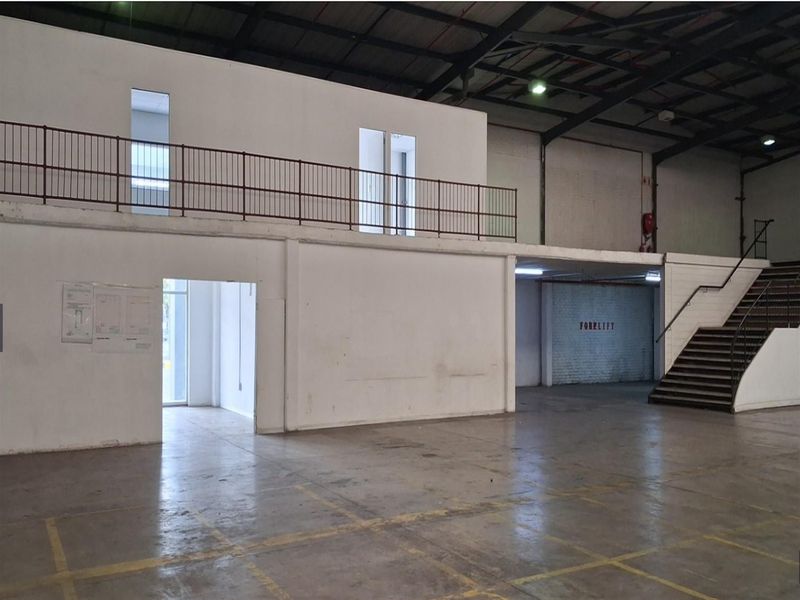Spacious industrial warehouse interior featuring a mezzanine level, metal staircase, exposed steel roof trusses, and durable concrete flooring.