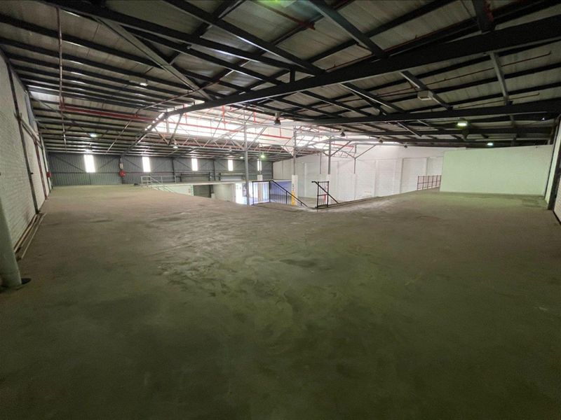 Spacious industrial mezzanine level featuring exposed steel roof trusses, concrete flooring, and metal wall cladding, suitable for storage or light industrial operations.