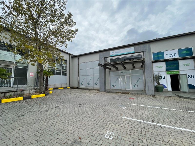 Front exterior view of an industrial property featuring a paved parking area, glass entrance doors, and a metal canopy structure.