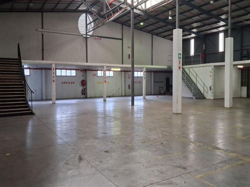 Spacious industrial warehouse featuring high ceilings with exposed steel trusses, concrete flooring, and a mezzanine level accessible via two steel staircases.
