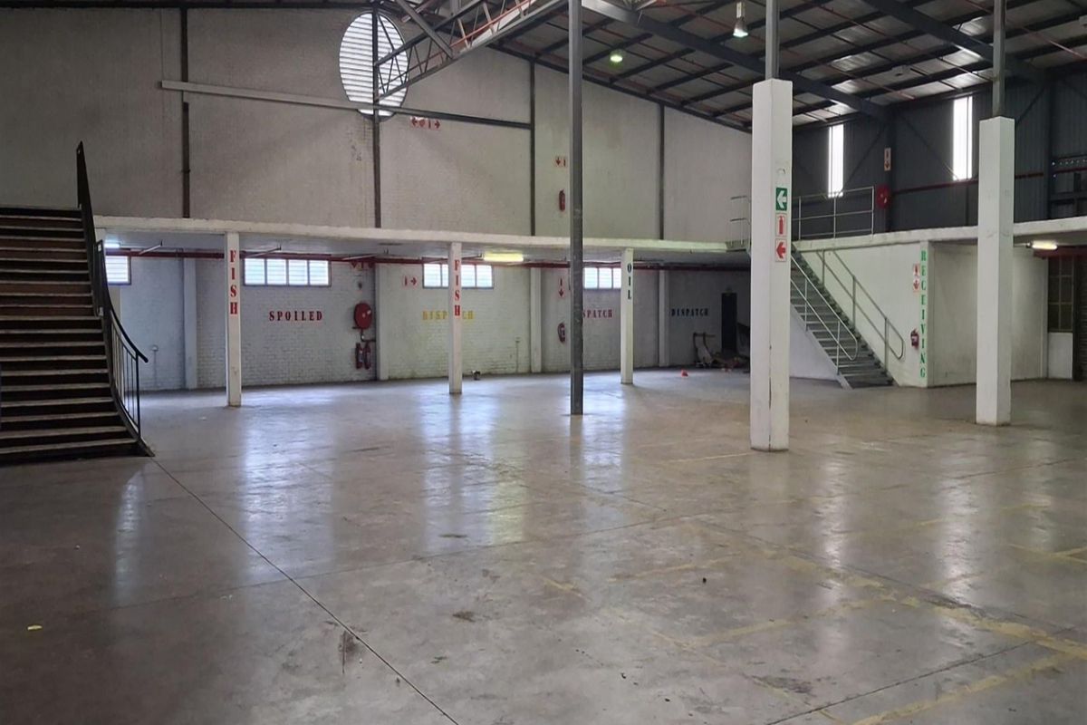 Spacious industrial warehouse featuring high ceilings with exposed steel trusses, concrete flooring, and a mezzanine level accessible via two steel staircases.