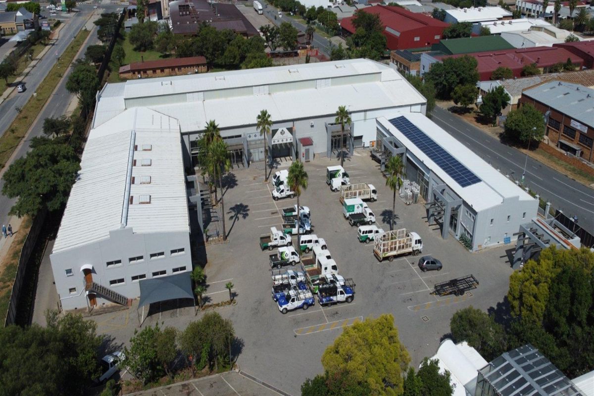 Aerial view of an industrial property complex featuring multiple warehouse buildings, solar panel installations, and a large paved parking yard.