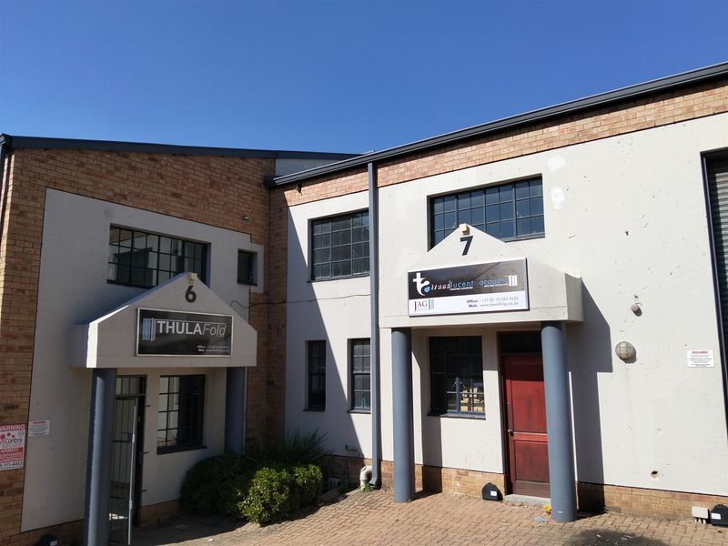 Front elevation of an industrial building featuring brick and plaster facade, steel-framed windows, and two distinct entrance porches with paved access.