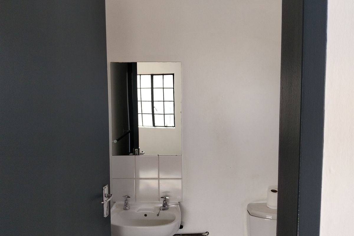 A functional bathroom featuring a wall-mounted basin with chrome taps, tiled splashback, wall mirror, and a standard toilet.