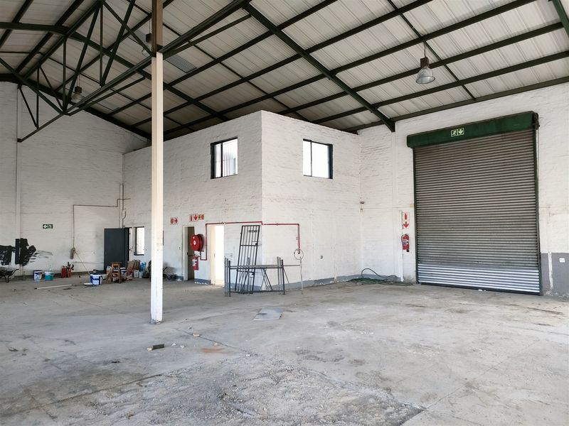 Spacious industrial warehouse unit featuring high ceilings with exposed steel trusses, a large roller shutter door, and essential fire safety equipment.