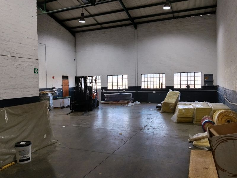 Spacious industrial warehouse unit featuring high ceilings with exposed steel trusses, concrete flooring, and large grid-style windows providing ample natural light.