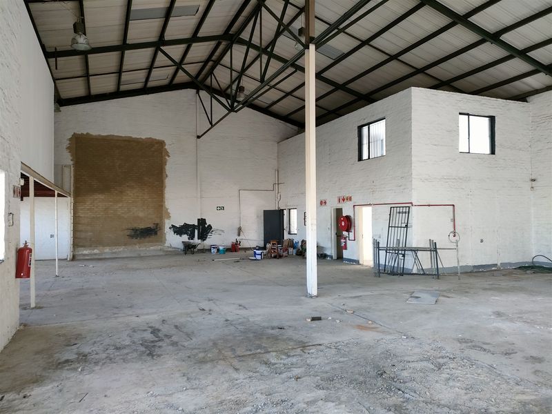 Spacious industrial warehouse unit featuring high ceilings with exposed steel trusses, concrete flooring, and integrated fire safety equipment.