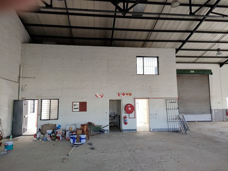 Spacious industrial warehouse area featuring high exposed steel roof trusses, a large roller shutter door, and essential fire safety equipment.
