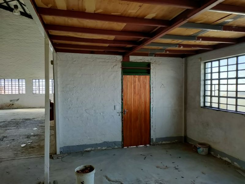 An industrial utility space featuring exposed steel beams, timber ceiling planks, steel-framed grid windows, and a solid timber door with concrete flooring.