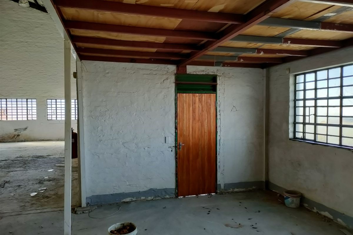 An industrial utility space featuring exposed steel beams, timber ceiling planks, steel-framed grid windows, and a solid timber door with concrete flooring.