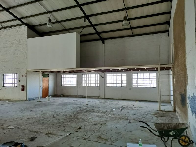 Spacious industrial utility area featuring a mezzanine level, steel roof trusses, grid windows, and durable concrete flooring, suitable for storage or workshop use.