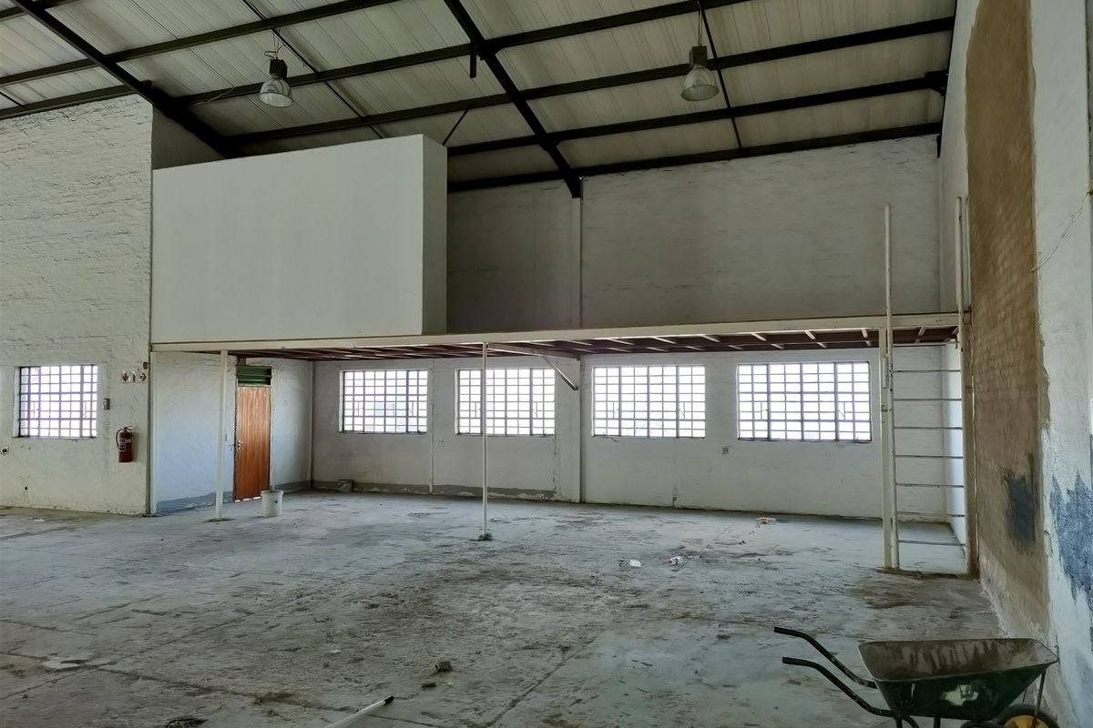 Spacious industrial utility area featuring a mezzanine level, steel roof trusses, grid windows, and durable concrete flooring, suitable for storage or workshop use.