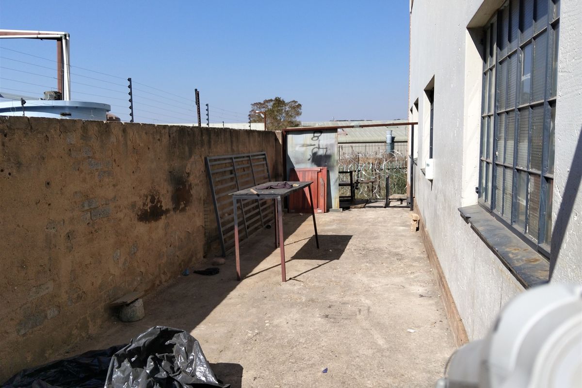 Rear exterior yard area featuring concrete paving, perimeter wall with electric fencing, and industrial steel-framed windows.