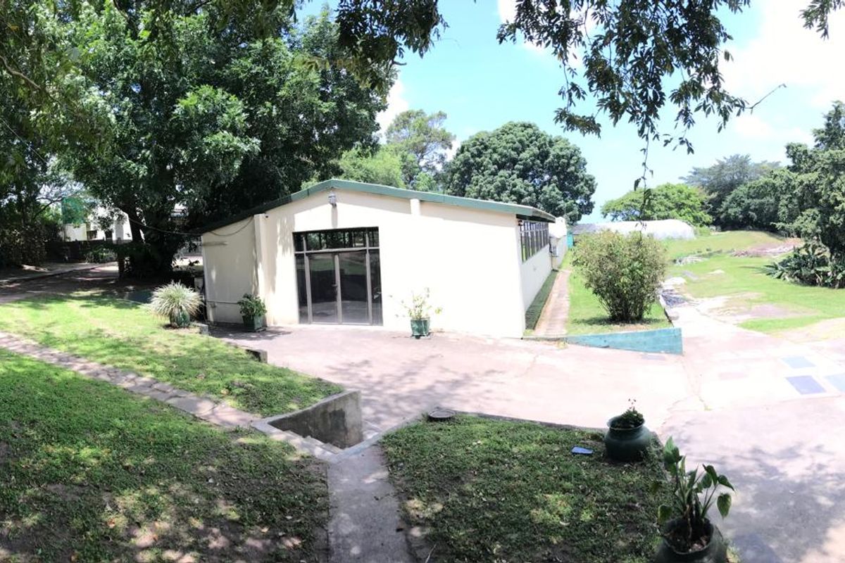 Rear view of the office building featuring a paved driveway, glass entrance doors, and surrounding landscaped garden area.