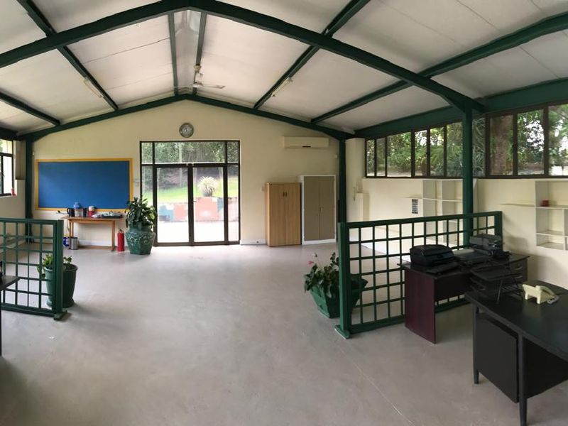 Spacious open-plan office area featuring exposed steel roof trusses, large windows for natural light, and built-in shelving units.