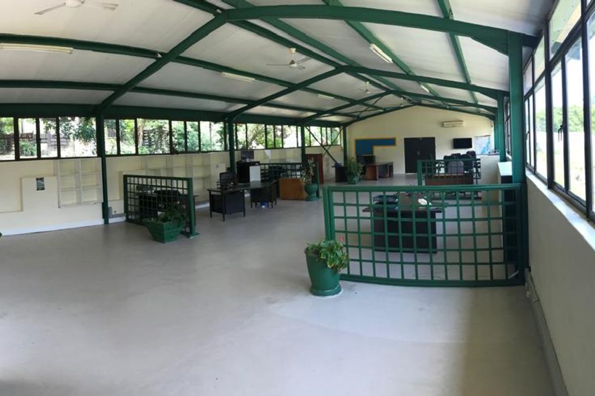 Spacious open-plan office area featuring high ceilings with exposed steel trusses, extensive natural light through large windows, and functional metal security partitions.