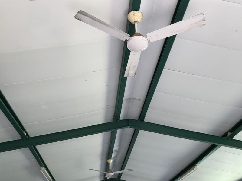Spacious office area featuring high vaulted ceilings with exposed green steel trusses, multiple ceiling fans, and integrated air conditioning.