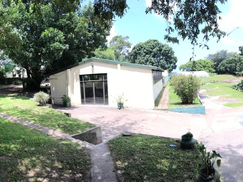 Rear view of the office building featuring a paved driveway, glass entrance doors, and surrounding landscaped garden area.