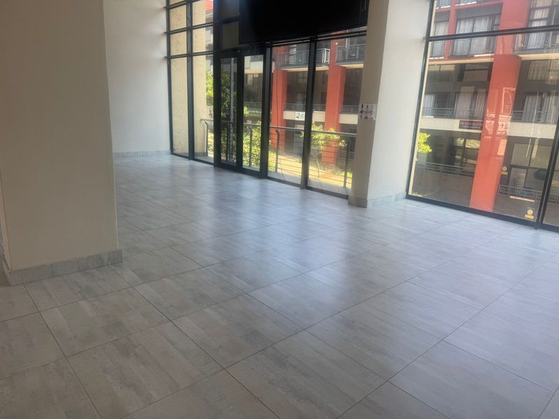 A bright, open-plan retail space featuring large floor-to-ceiling glass windows, modern grey tiled flooring, and a clean, minimalist interior layout.