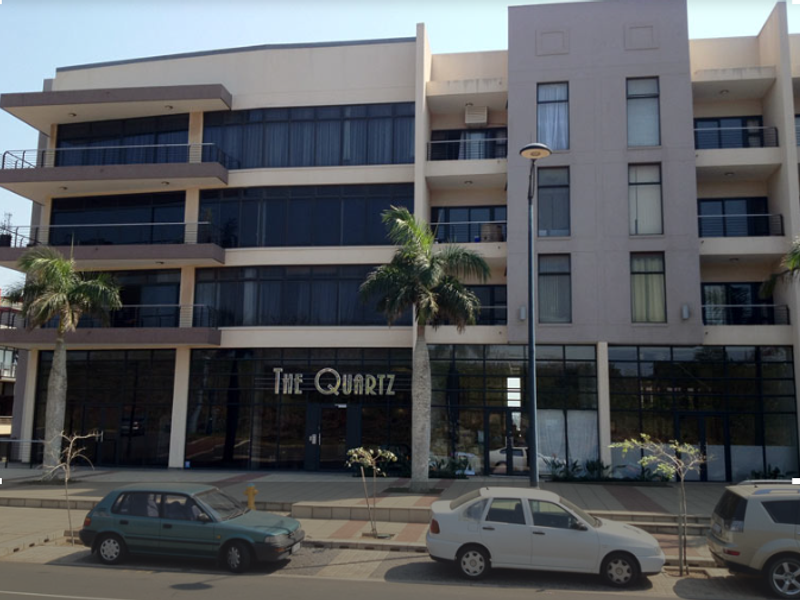 Modern multi-story retail and residential building facade featuring large glass storefronts, balconies with metal railings, and contemporary architectural design.