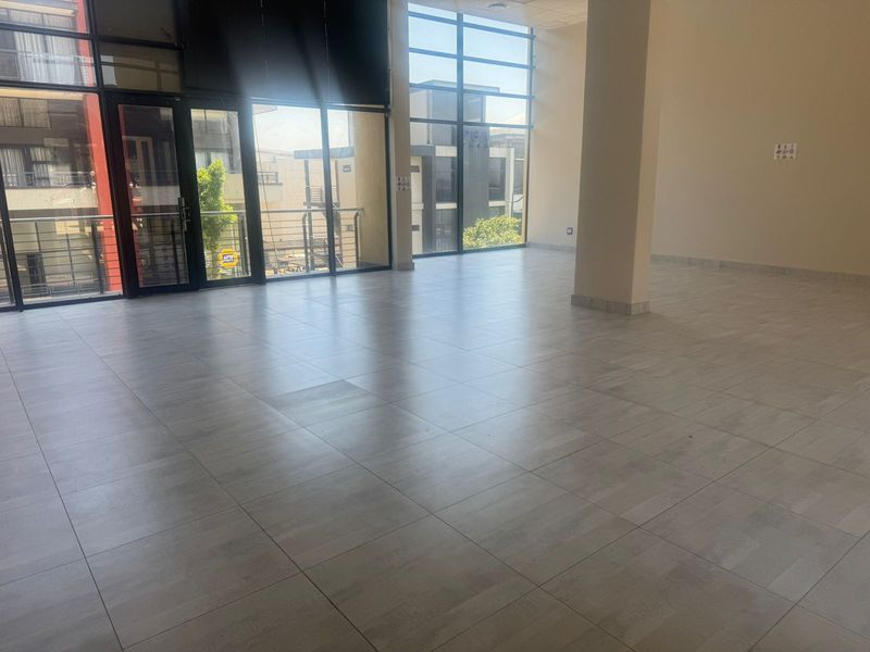 A bright, open-plan retail space featuring large floor-to-ceiling windows, tiled flooring, and a central structural column, offering a versatile layout for business use.
