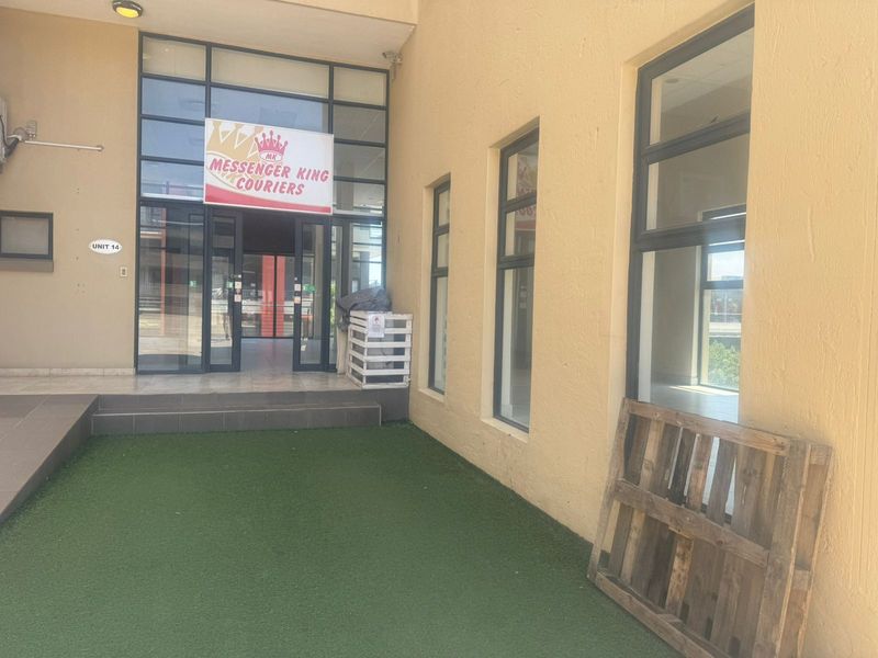 Exterior view of a commercial retail unit entrance featuring large glass windows, a glass door, and a small artificial grass area.