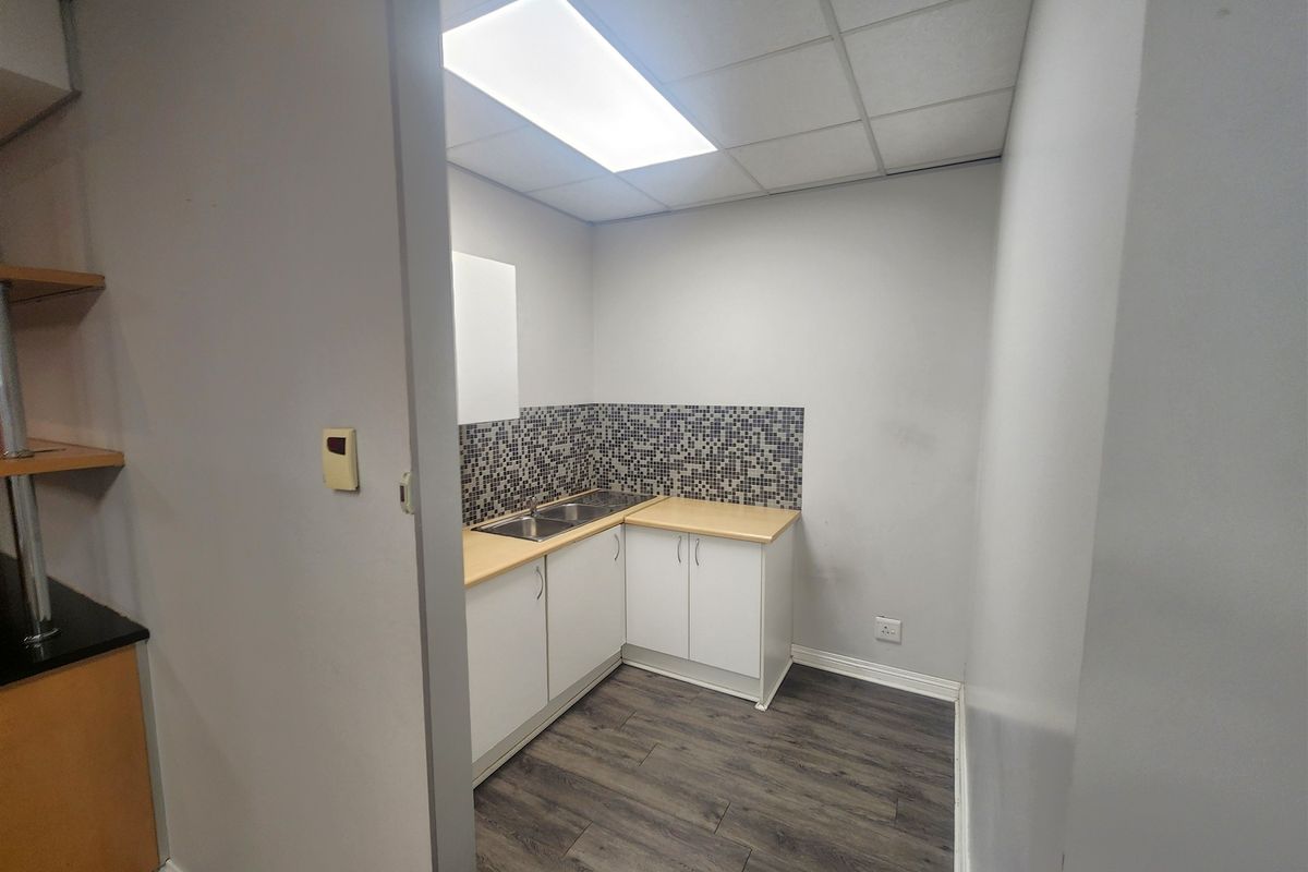 A compact office kitchenette featuring white cabinetry, laminate countertops, a stainless steel double sink, and a modern mosaic tile backsplash.