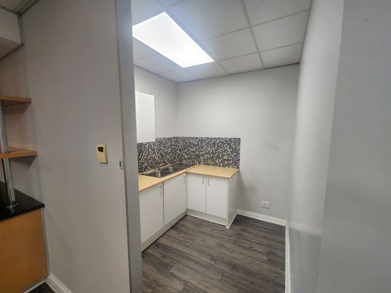 A compact office kitchenette featuring white cabinetry, laminate countertops, a stainless steel double sink, and a modern mosaic tile backsplash.