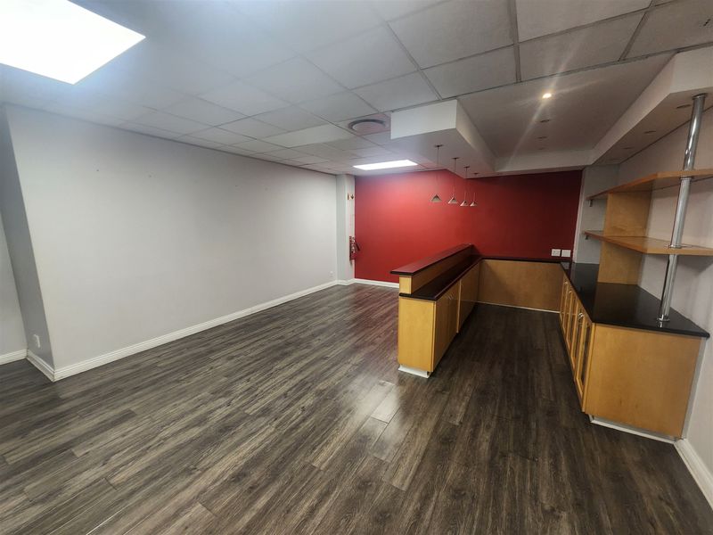 Spacious office area featuring modern laminate flooring, a suspended ceiling with recessed lighting, and a built-in service counter with storage cabinetry.