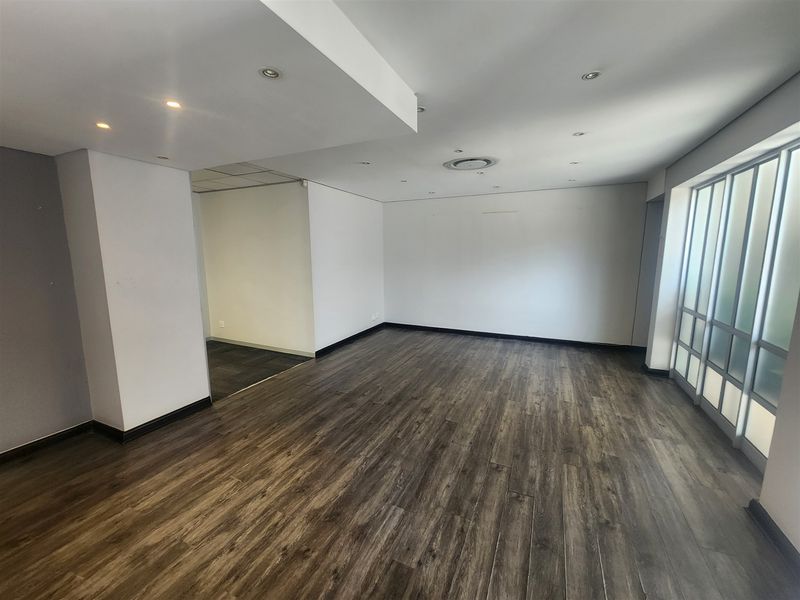 A spacious, empty office area featuring modern laminate flooring, recessed ceiling lighting, and a large frosted glass partition wall.
