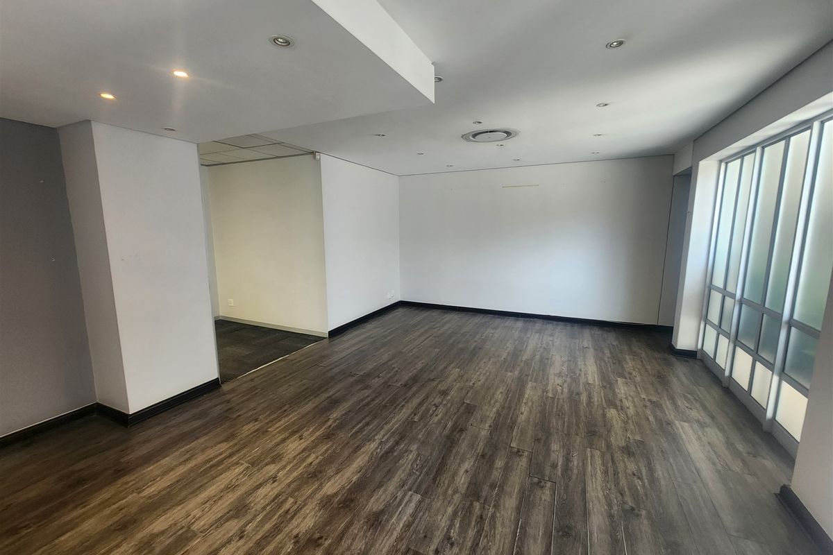 A spacious, empty office area featuring modern laminate flooring, recessed ceiling lighting, and a large frosted glass partition wall.