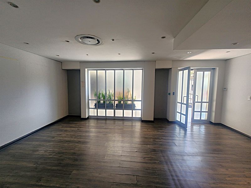 A bright, open-plan office space featuring dark wood-look flooring, recessed ceiling lighting, and a modern frosted glass partition with an integrated glass door.