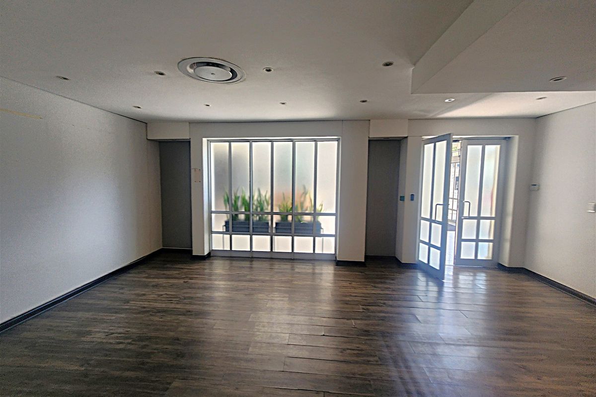 A bright, open-plan office space featuring dark wood-look flooring, recessed ceiling lighting, and a modern frosted glass partition with an integrated glass door.