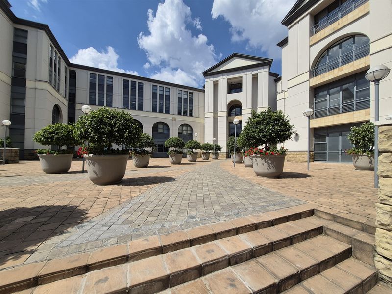 A well-maintained paved courtyard area between office building wings, featuring stone steps, integrated exterior lighting, and professional landscaping.