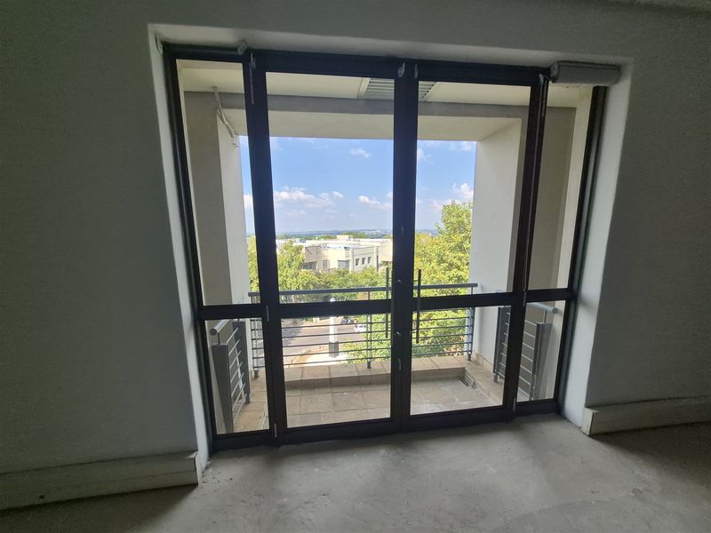 A view from an interior office space looking out through double glass doors onto a private balcony with metal railings and urban views.
