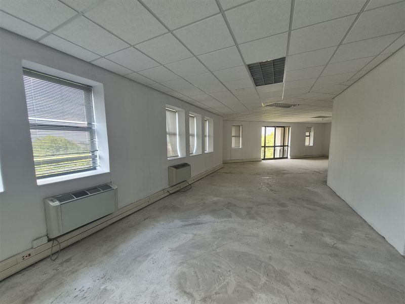 Spacious, open-plan office area featuring a suspended ceiling, recessed lighting, multiple windows with blinds, and wall-mounted HVAC units, ready for custom flooring installation.